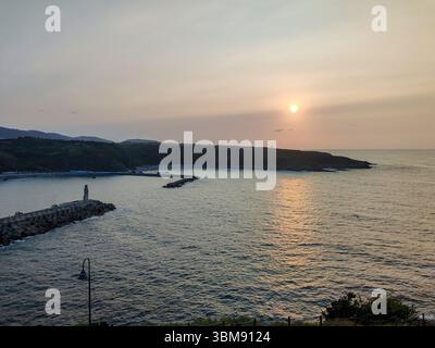 Golden Hour beleuchtet eine friedliche Bucht mit einem Leuchtturm, der vor der felsigen Küste wacht Stockfoto