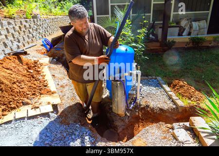 Der Klempner arbeitet an der Einrichtung der Wasserbrunnenpumpe im Freien und verbessert den Wohnbereich während des Arbeitstages Stockfoto