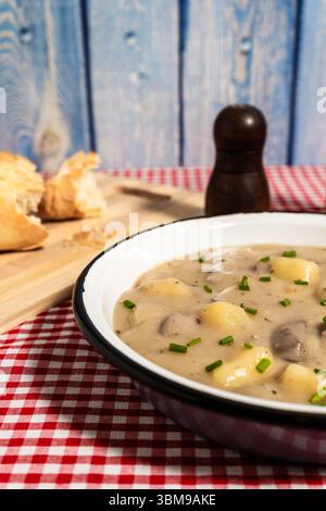 Pilzsuppe mit Kartoffeln und Schnittlauch, serviert in einer Schüssel auf einer karierten Tischdecke, perfekt für eine wohltuende Mahlzeit Stockfoto