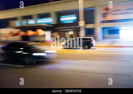 Bewegungsunschärfe eines gelben Fahrerhauses, das durch eine Nachtstraße in Taipei fährt und die pulsierende urbane Atmosphäre und das dynamische Stadtleben einfängt. Stockfoto