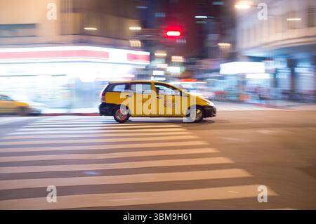 Bewegungsunschärfe eines gelben Fahrerhauses, das durch eine Nachtstraße in Taipei fährt und die pulsierende urbane Atmosphäre und das dynamische Stadtleben einfängt. Stockfoto