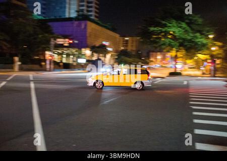 Bewegungsunschärfe eines gelben Fahrerhauses, das durch eine Nachtstraße in Taipei fährt und die pulsierende urbane Atmosphäre und das dynamische Stadtleben einfängt. Stockfoto