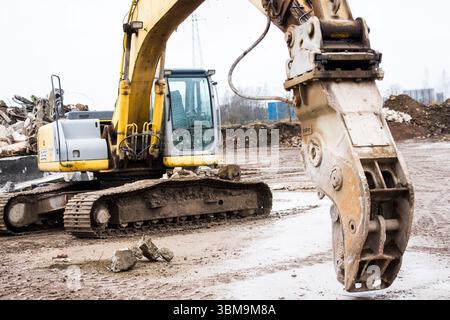 Nahaufnahme eines leistungsstarken gelben Abbruchbaggers mit speziellem Betonbrecher oder Pulverisiergerät an einer Konstruktion oder einem Abbruch Stockfoto