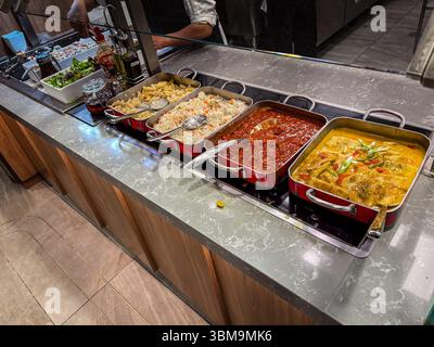 Selbstbedienungsbuffet mit verschiedenen warmen Speisen, Salatbar und Gewürzen für Gäste, die ihre eigene Mahlzeit wählen können. Stockfoto