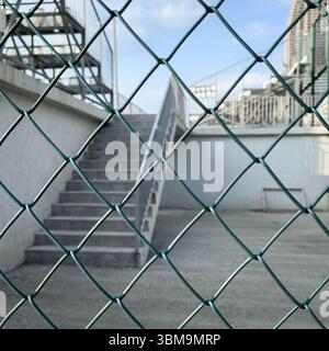 Betontreppe umrahmt von Metalldrahtzaun, urbaner Minimalismus. Konzeptionelle Sicht für Architektur, Psychologie und redaktionelle Nutzung. Stockfoto