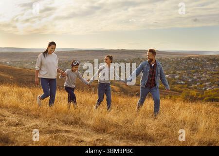 Glückliche Mutter, Vater, Sohn und Tochter gehen zusammen auf dem Feld und halten die Hände Stockfoto
