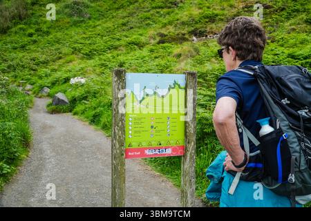 Wandererin mit Rucksack, die sich ein Wegweiser für den Red Trail in der Nähe des Giant's Causeway in Nordirland anschaut. Stockfoto