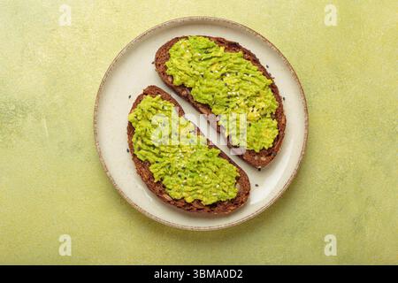 Zwei Scheiben Avocado Toast mit Sesamsamen auf Roggenbrot, Blick von oben auf hellgrünem Hintergrund Stockfoto