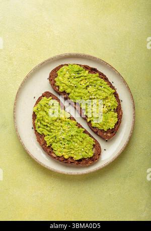 Zwei Scheiben Avocado Toast mit Sesamsamen auf Roggenbrot, Blick von oben auf hellgrünem Hintergrund Stockfoto