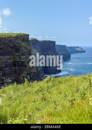 Cliffs of Moher, Irland. Dramatische Küstenklippen treffen an einem sonnigen Tag mit grünem Gras im Vordergrund auf den atlantik. Stockfoto