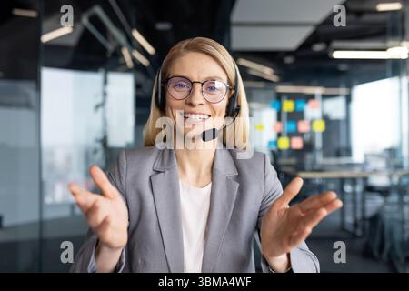 Ein freundlicher Kundendienstmitarbeiter, der ein Headset in einer modernen Büroumgebung trägt, lächelnd und gespenstisch wirkt. Stockfoto