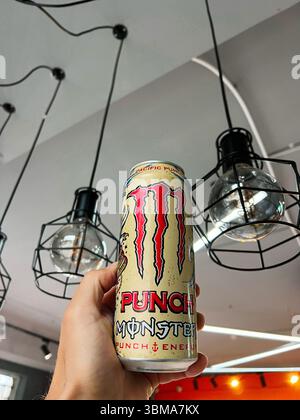 Kiew, Ukraine - 24. Juni 2025: Person mit einem Monster Punch Energy Drink unter dekorativen Deckenleuchten in einem Café. Stockfoto
