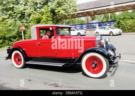 Ein roter Klassiker von Packard mit weißen Reifen, der mit einem Mann im Inneren eine Kappe trägt, die Straße hinunter fährt Stockfoto