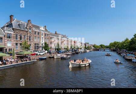 Haarlem, Niederlande (21. Juni 2025) - Ein malerischer Wasserkanal bietet Boote mit Menschen, die den sonnigen Tag genießen. Gesäumt von historischen niederländischen Häusern Stockfoto