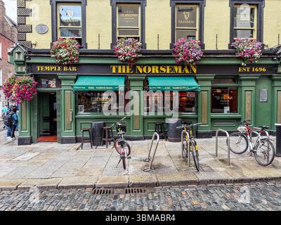 Die Fassade des Norseman Pubs im Stadtteil Temple Bar von Dublin. Ein altes Gebäude mit Blumenkörben, Fahrrädern und Menschen auf einer Kopfsteinpflasterstraße. Stockfoto