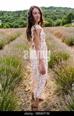Frau im Blumenkleid, die im Sommer im Lavendelfeld steht Stockfoto