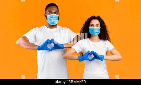 Paar Gestikulierenden Herzform Tragen Masken Und Handschuhe, Gelber Hintergrund Stockfoto