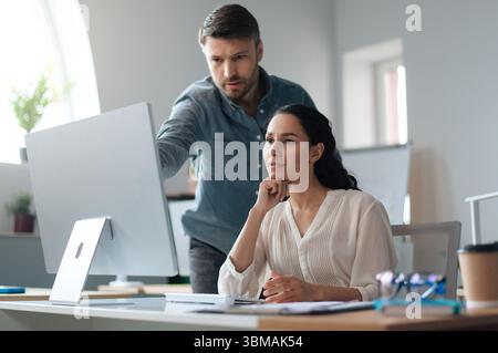 Junge Auszubildende, die zusammen mit ihrer Geschäftsbetreuerin am modernen Unternehmensbüro am Computer arbeitet Stockfoto