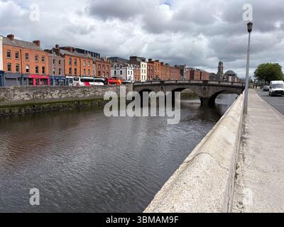 James Joyce Bridge. Moderne Fußgängerbrücke über den Fluss Liffey in Dublin, Irland, mit historischen Gebäuden entlang des Kais an einem bewölkten Tag. Stockfoto