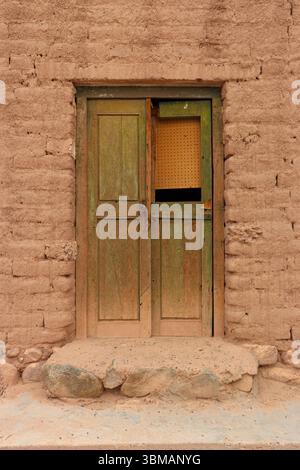 Alte, verwitterte Holztür in einer lehmwand, die die traditionelle Architektur von Fiambala, Catamarca, zeigt. Stockfoto