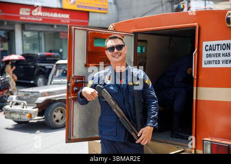 13. Mai 2025: Calapan City, Philippinen, ein lächelnder bewaffneter Sicherheitsbeamter, der in der Nähe eines gepanzerten Lastwagens in der Stadtstraße steht Stockfoto