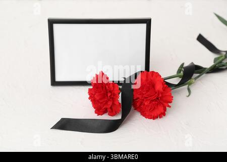 Leerer Trauerrahmen, Nelkenblumen und leeres Band auf hellem Hintergrund Stockfoto