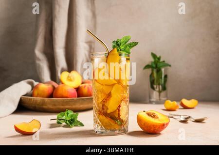 Glas leckerer Pfirsicheistee auf rosa Grunge Hintergrund, Nahaufnahme Stockfoto