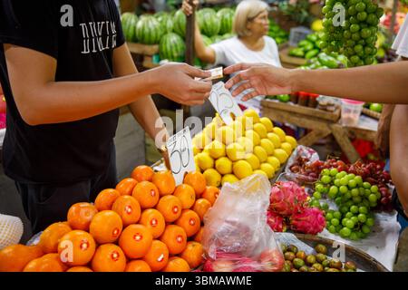 13. Mai 2025: Calapan City, Philippinen, Nahaufnahme der Hände, die mit Bargeld auf dem Obstmarkt mit Orangen Zitronen Trauben und Drachenfrüchten bezahlen Stockfoto