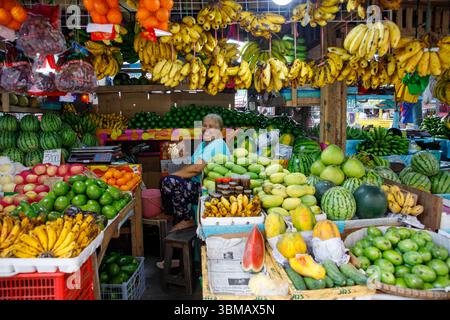 13. Mai 2025: Calapan City, Philippinen, lächelnde ältere Verkäuferin, die Bananen, Mangos, Wassermelonen und lokale tropische Produkte am Marktstand verkauft Stockfoto