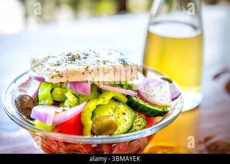 Griechische Salatschale, traditionelle hausgemachte Mahlzeit Vorspeise auf Ikaria Griechenland, Kathoura Schafskäse, Gemüseflasche Weißwein im Hintergrund Stockfoto