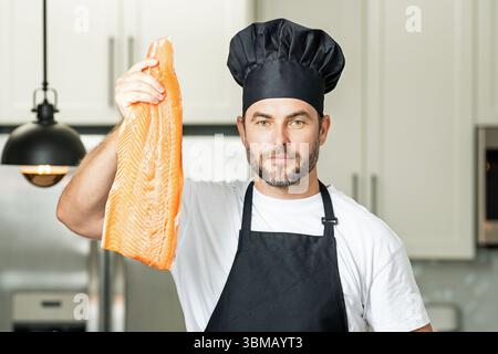 Koch in einheitlicher Küche rohes Fischlachsfilet in der Küche. Restaurantmenü-Konzept. Männlicher Koch in Arbeitsuniform, schwarze Schürze, Kochmütze. Fisch Stockfoto