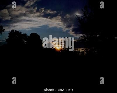 Ein wunderschöner, ruhiger Blick auf den Sonnenuntergang mit Silhouetten von Bäumen vor einem atemberaubenden, dramatischen Himmel voller Wolken Stockfoto