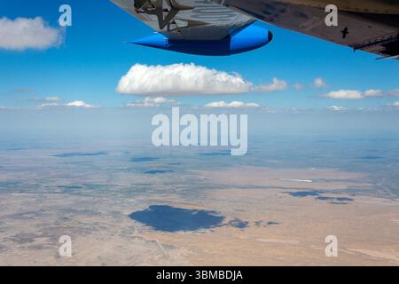 Die Luftperspektive fängt die Weite der usbekischen Wüste ein, eingerahmt von einem Flügel eines Flugzeugs, unter einem hellblauen Himmel mit flauschigen Wolken. Stockfoto