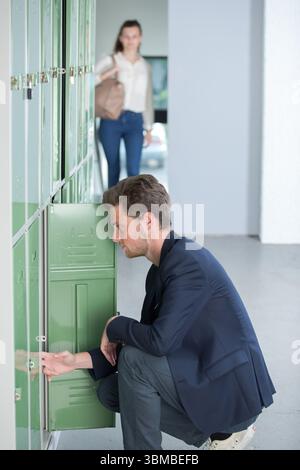 Ein junger, gutaussehender Mann öffnet die Schließfachtür aus Metall Stockfoto