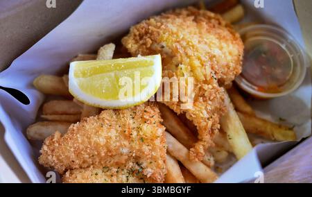 Klassisches traditionelles englisches oder britisches kulinarisches Delikatessen Fish and Chips, goldener, frittierter Fisch mit Zitronenscheiben in einer Papierkarton zum Mitnehmen als Mittagessen Stockfoto
