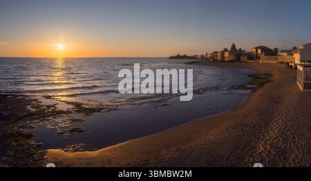 Die goldene Sonne taucht in Punta Secca in den Horizont ein, reflektiert auf dem ruhigen Wasser und strahlt ein warmes Leuchten an der Küste in Sizilien, Italien Stockfoto