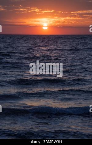 Goldene Farbtöne verschmelzen mit sanften Wellen, während die Sonne am Horizont absinkt und ein friedliches Leuchten über dem Ozean ausstrahlt. Stockfoto