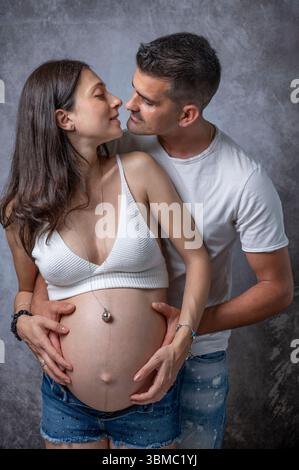 Ein Mann umarmt und ist dabei, seinen Partner zu küssen, der schwanger ist Stockfoto