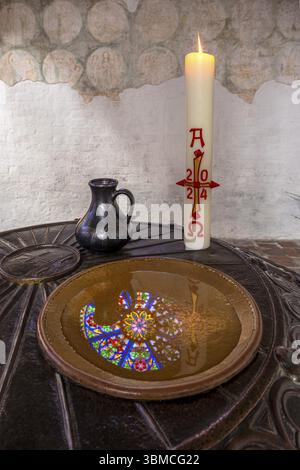 Ein farbenfrohes rundes Buntglasfenster im nördlichen Querschiff des St. Maria- und Johannisdoms in Schwerin spiegelt sich in der bronzenen Taufe von Stockfoto