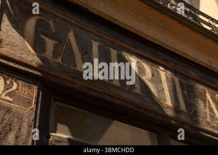 Eine detaillierte Nahaufnahme zeigt ein verwittertes, antikes Schild mit der Aufschrift „Galerie“ auf einer dunkelbraunen Holzfassade. Stockfoto
