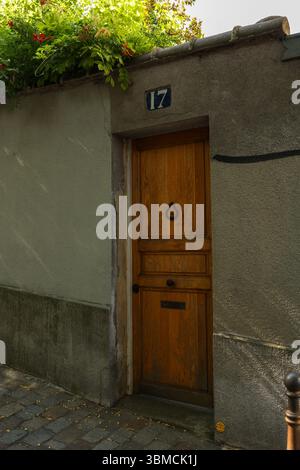 Ein Foto einer alten Holztür in einem verwitterten Gebäude in Paris, Frankreich. Die Nummer 17 ist über der Tür zu sehen. Kletterpflanzen mit lebendigem R Stockfoto