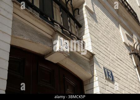 Eine detaillierte Nahaufnahme erfasst die Nummer 13 auf einem verwitterten, weißen Backsteingebäude. Die dunkelbraune Holztür und der verzierte Metallbalkon Stockfoto