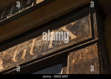 Eine detaillierte Nahaufnahme zeigt ein verwittertes, Vintage-Ladenschild an der Außenseite eines alten Gebäudes. Das Schild mit verblasster Schrift, hin Stockfoto