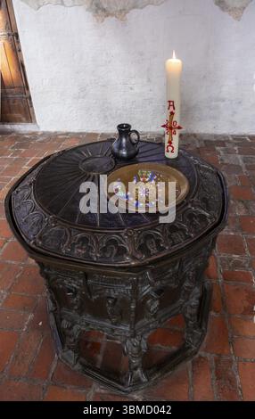 Ein farbenfrohes rundes Buntglasfenster im nördlichen Querschiff des St. Maria- und Johannisdoms in Schwerin spiegelt sich in der bronzenen Taufe von Stockfoto