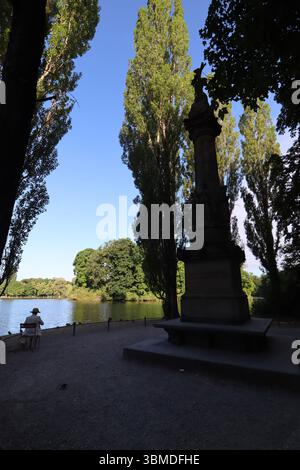 MÜNCHEN, DEUTSCHLAND - 24. JUNI 2025: Statue, die im Morgenlicht am Eingang des Hofgartens umrahmt von hohen Bäumen und reflektiert wird Stockfoto