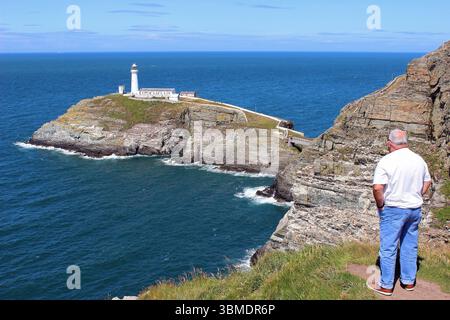 Senior Mann mit Blick in Richtung South Stack Lighthouse, Anglesey, Wales Stockfoto