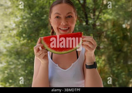 Glückliche junge Frau, die saftige Wassermelonenscheibe mit Glitzer-Make-up und geflochtenem Haar hält Stockfoto
