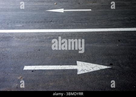Weiße Richtungspfeile auf Asphalt-Fahrbahnoberfläche gemalt. Stockfoto