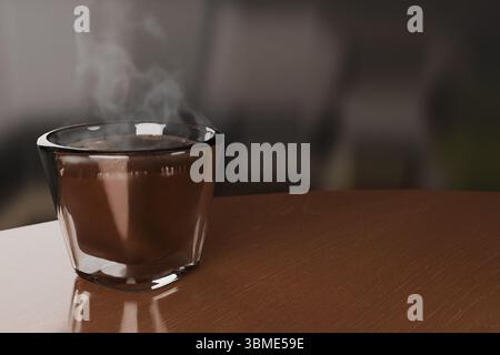 Ein Close-up-Studio zeigt einen dampfenden heißen Espresso, der in einem klaren, doppelwandigen Thermoglas auf einer Holzoberfläche serviert wird. Sichtbar Stockfoto