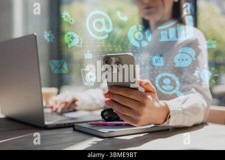 Geschäftsfrau mit Smartphone und Laptop am Schreibtisch, umgeben von digitalen Marketing- und KI-Symbolen. Konzept Der Modernen Technologie, Kommunikation, Daten Ana Stockfoto